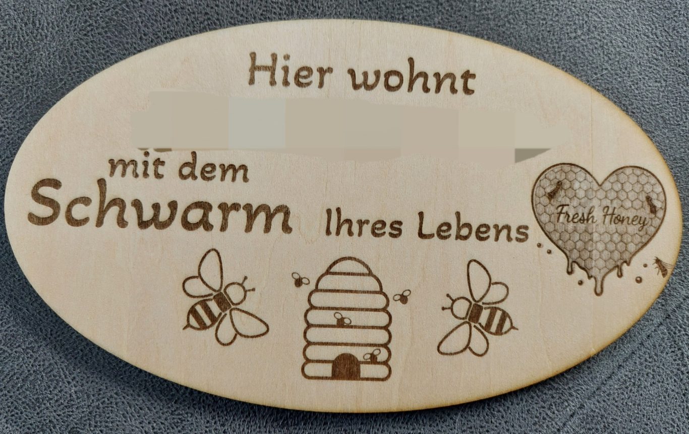 Holzschild mit Aufschirft "Hier wohnt XxX mit dem Schwarm Ihres Lebens" und Bienenmotiven Holzschild mit Inschrift „Hier wohnt mit dem Schwarm ihres Lebens“ und Bienenmotiven.